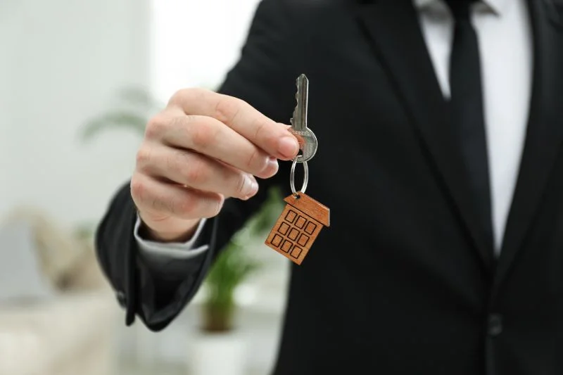 Person offering house key with keychain.