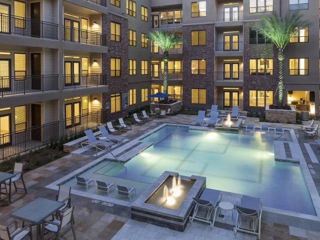 Apartment complex pool area at dusk with lights on.