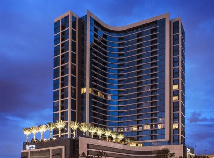 Modern high-rise hotel building at dusk with lit palms