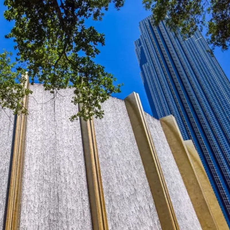 Urban waterfall feature with skyscraper and trees.