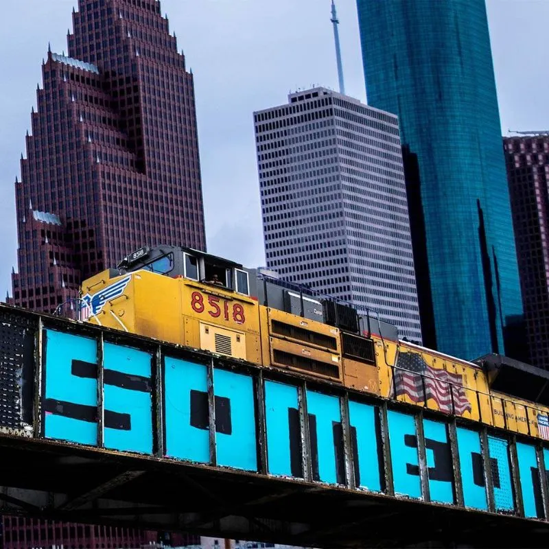 Freight train crossing graffiti bridge in urban skyline.